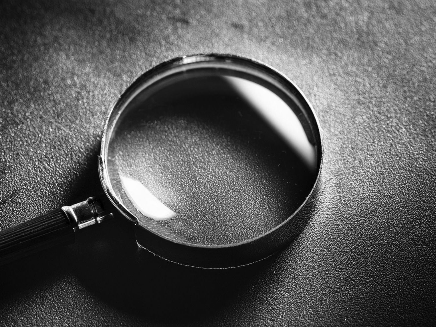 Black-and-white close-up of a magnifying glass on a dark, textured surface.