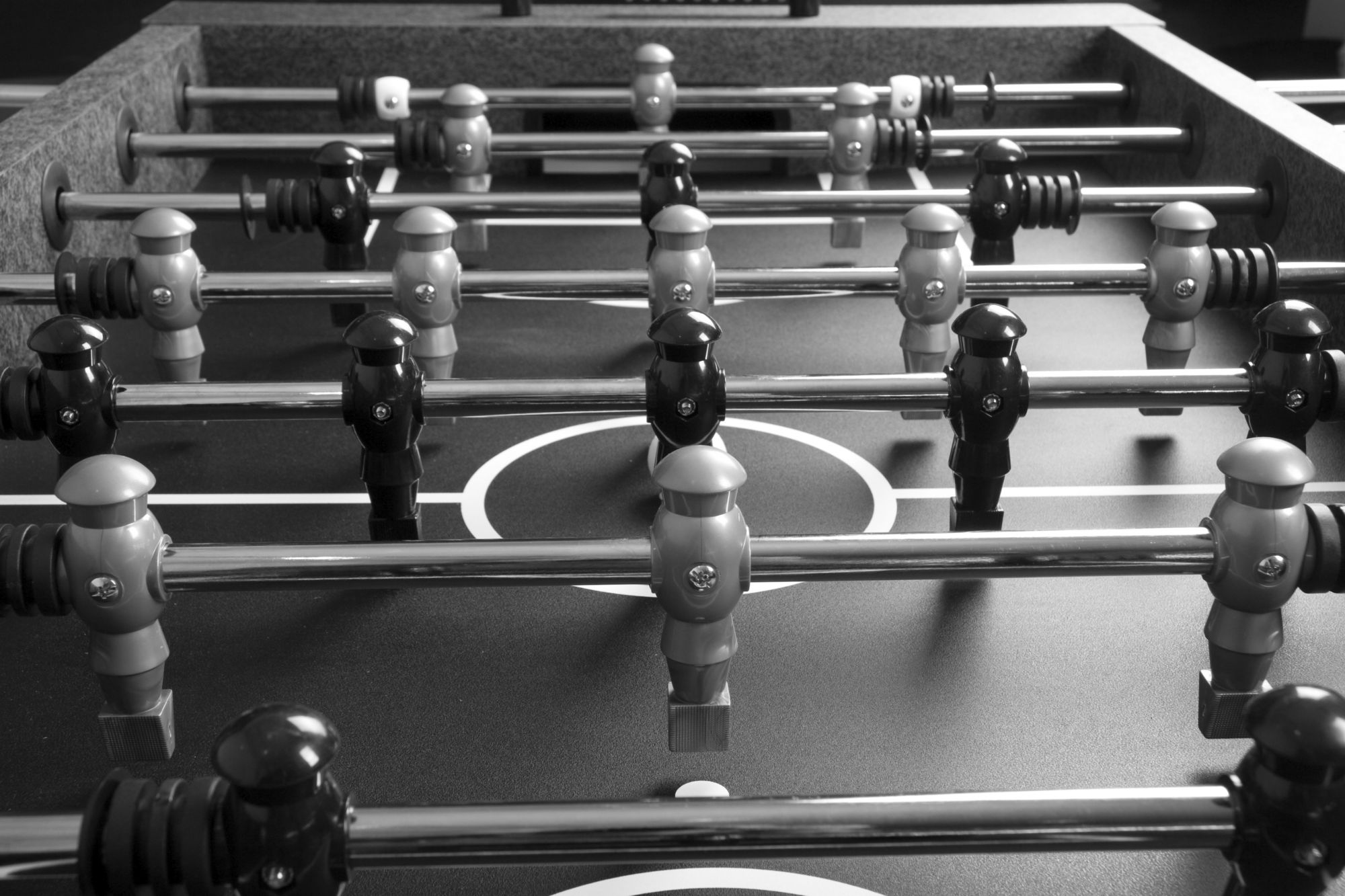 Black-and-white close-up of a foosball table with several rows of dark and light players on metal rods.