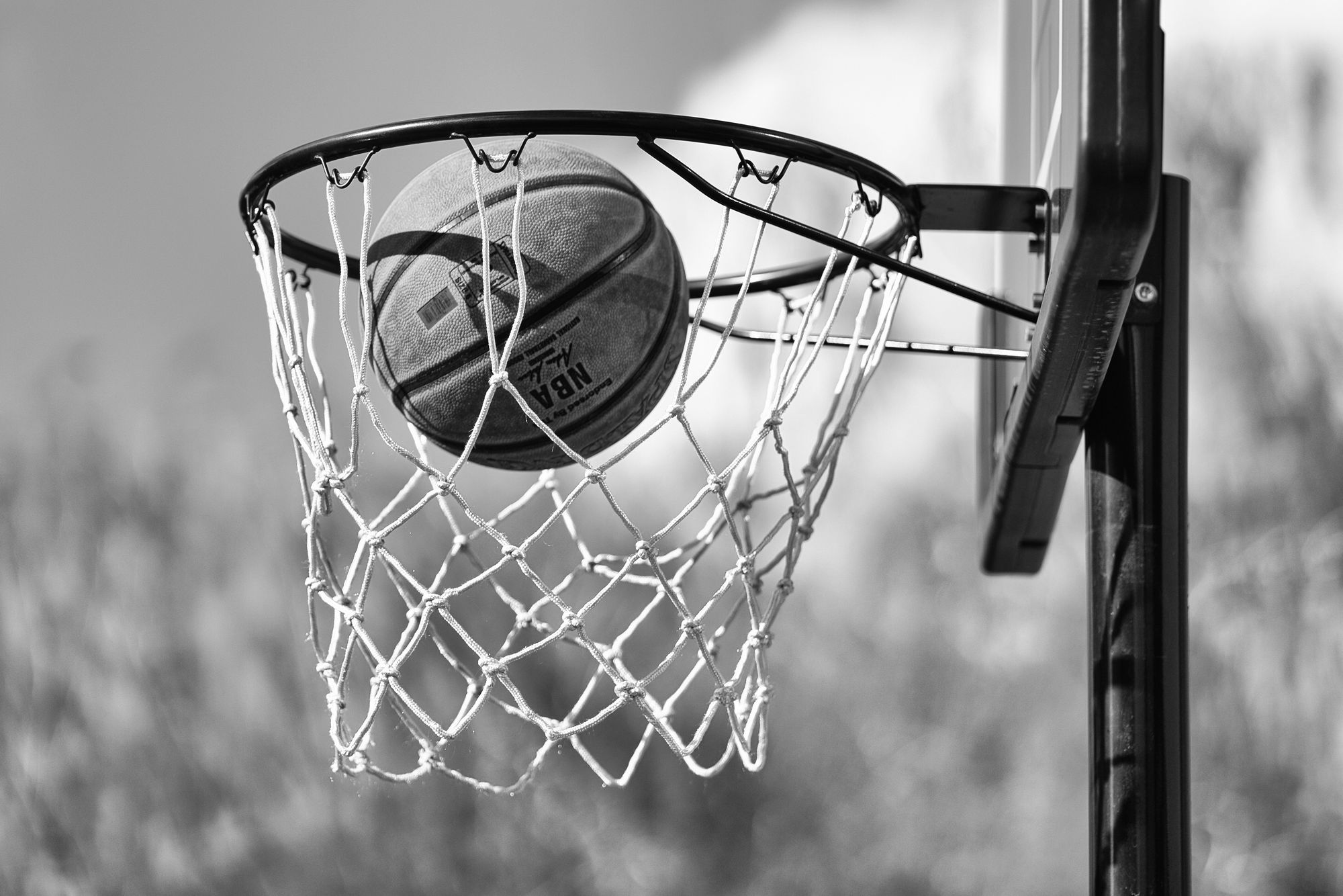 Black-and-white image of a basketball stuck in a basketball hoop's net.