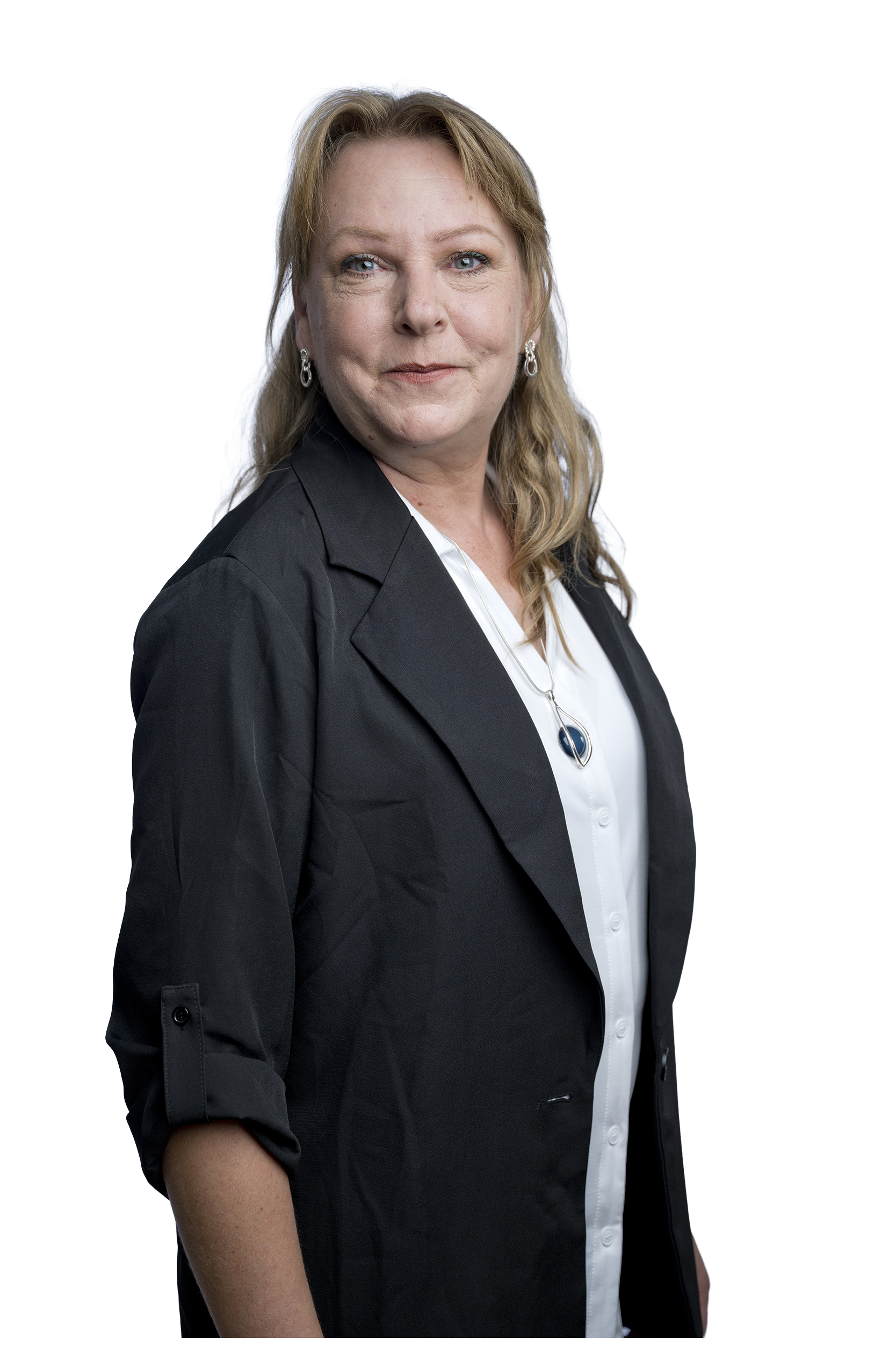 Porträt einer Frau mit schulterlangem blondem Haar, schwarzem Blazer, weißer Bluse und Schmuck vor hellblauem Hintergrund.