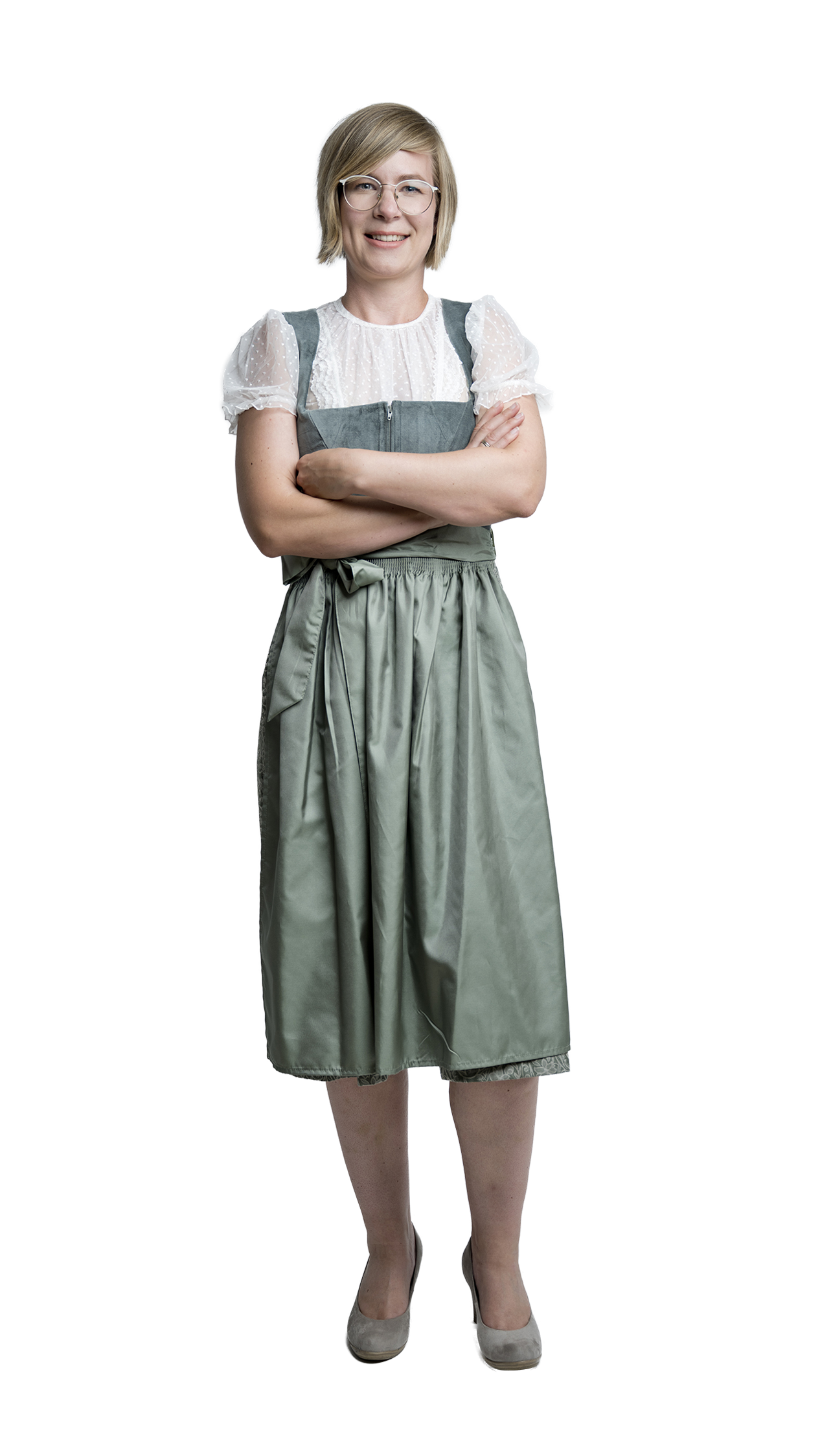 Ganzkörperaufnahme einer lächelnden Frau mit Brille, die in einem grünen Dirndl mit weißer Bluse und verschränkten Armen vor hellem Hintergrund steht.