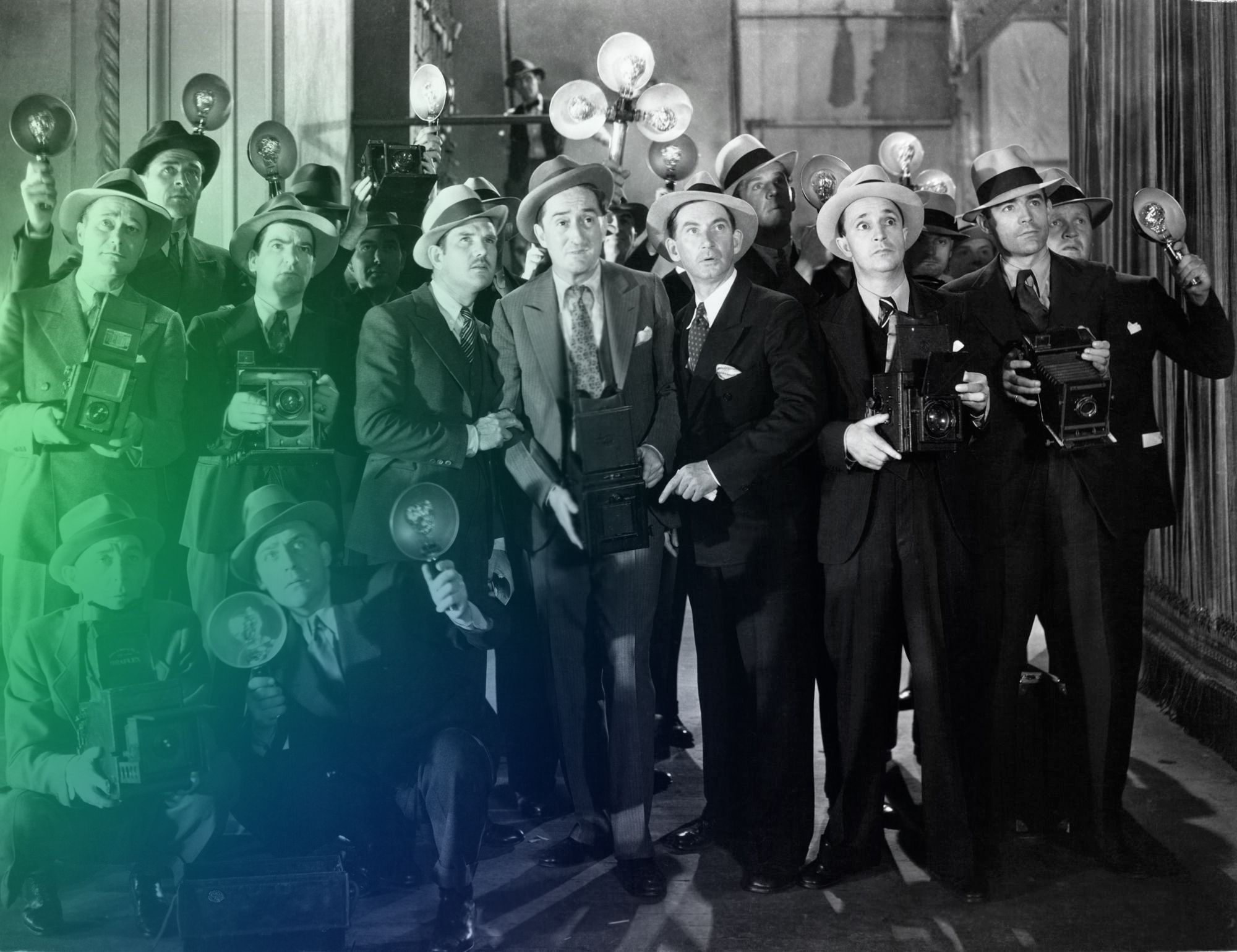Black-and-white photograph of a group of men in suits and hats holding old cameras and flash devices.