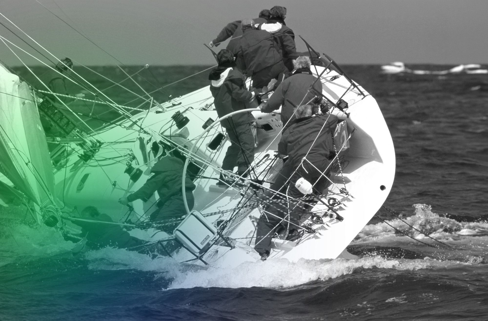 Several sailors try to stabilize a sharply tilted sailboat in rough seas.